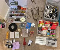 Overview photo displaying an assortment of small household tools and parts spread on floor including cords, hardware, sanding block, tape measure, staples, and light fixtures.