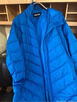 Bright blue puffer coat hung on hanger showing front with zipper and high collar