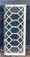 Full view of antique transom window showing original wavy glass with diamond and rectangular muntin design, painted wooden frame with multiple layers of old paint.
