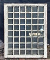 Photo of an antique transom window showing original wavy glass with a white painted solid wooden frame and a grid of small panes.