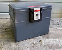 Closed gray metal First Alert fire safe on outdoor surface, showing front locking mechanism and brand label.