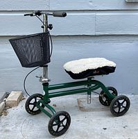 Side view of a green foldable knee scooter with black mesh basket, padded knee platform with removable wool cover, and hand brake.