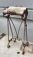Front view of the wrought iron and marble side table showing the ornate rusty metal base and square marble top.