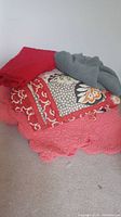 Three blankets stacked together - red quilted, floral pattern, and grey knit blanket visible