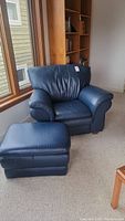 Blue leather armchair and matching ottoman positioned near a window and bookshelf.