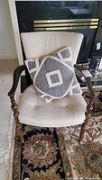 Full view of the vintage upholstered chair with a black and white geometric throw pillow placed on the seat, showing the overall condition and style.