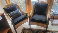 Two rattan wicker armchairs with black seat and back cushions and one striped lumbar pillow shown together