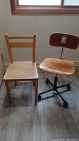 Two chairs next to each other: one wooden chair with rattan seat, one adjustable wooden seat office chair with caster wheels.