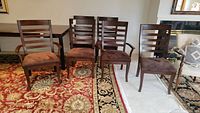 Full view of the 6 dining chairs showcasing 2 captains chairs with arms and 4 armless side chairs. Wooden frame with horizontal slat backs. Brown upholstered seats.