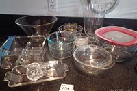 Overview of all glass dishware items on counter including bowls, trays, condiment dishes, and storage container with lid