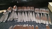 Grouped dining knives, forks, and spoons laid out in lines on a dark surface.