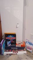Photo showing stacked board games including Monopoly, Pictionary, Clue, Backgammon, Dictionary book, and children's books.