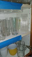 Shelf showing clear glass and textured plastic/acrylic drink glasses, some are tumblers and some are stacked cups.