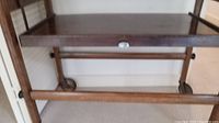 Close-up photo of the base showing the wheels and lower shelf structure of the antique wooden table.