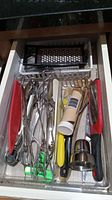 Top view of assorted kitchen utensils stored in a drawer including graters, tongs, peelers, and other small tools.