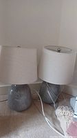 Two round ceramic base table lamps with white drum shades on floor near wall.