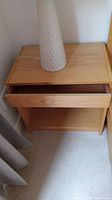 Photo of one wooden nightstand with drawer slightly open, light-colored wood with natural finish, showing scratches and used condition.