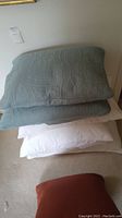 Stack of pillows showing 2 blue quilted shams on top of 4 white bed pillows