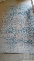 Full view of blue and white patterned rectangular rug on floor showing worn condition