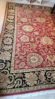 Red and black traditional style area rug with large floral and paisley designs, detailed floral black border, and beige trim with fringe edges.
