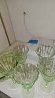 Five green etched ribbed glass goblets arranged together