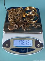 Photo of a collection of tangled and stacked gold filled jewelry pieces on a digital scale showing weight 176.13 grams.