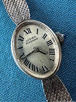 Close-up front view of oval dial with Roman numerals and 'Lucien Piccard' branding on silver-tone face with textured gold filled band.