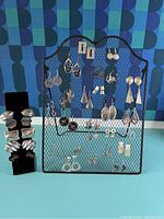 Front view of two black mesh earring display holders showing a variety of sterling silver earrings in different styles including hoops, dangles, and abstract shapes.