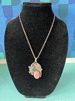 Front view of silver necklace with pendant featuring pink stone displayed on black mannequin bust.
