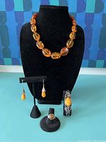 Full set of five amber jewelry pieces: necklace, earrings, ring, and bracelet displayed on black holders