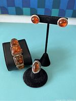 Four jewelry pieces displayed: bracelet, ring, earrings shown with black velvet holders on turquoise background