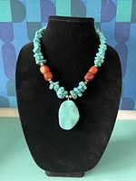 Front view of the chunky turquoise and carnelian bead necklace with large turquoise pendant on black display bust.