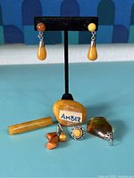 Overall view of the set items including drop earrings on display stand, amber bar pin, oval decorative pin/ring, and pendant.