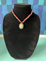 Front view of necklace on black display showing coral and turquoise beads and oval turquoise pendant.