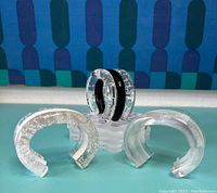Three lucite bangles displayed on clear acrylic stand showing front and side profiles