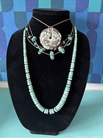 Front view of five turquoise necklaces displayed on black bust, showing bead strand and multi-strand designs with round pendant.