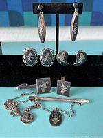 Full lot view showing earrings on display stand and various pendants, cufflinks, and tie clips laid out in front.