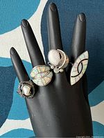 Four rings displayed on black hand form, front view