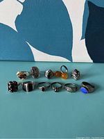 Lot of 11 assorted sterling silver rings displayed in two rows, showing variety of sizes and stone colors including black, orange, and blue.