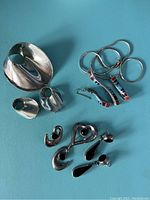 Various sterling silver jewelry pieces including pins, earrings, and necklaces with modern abstract designs and colored inlays.