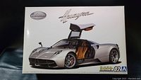 Box front image of the Aoshima Pagani Huayra '12 1/24 model kit showing the silver car with gull-wing door open and tan interior.