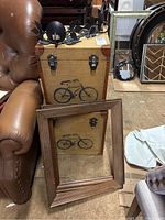 Photo showing two decorative storage boxes stacked with bicycle print, metal latches, and a wooden frame propped in front.