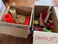 Photo of two open boxes, one labeled 'ELECTRIC CANDLES' containing battery operated candles in red and white, and another labeled 'CANDLES' with various taper and votive candles.