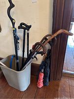 Photo of an assortment of canes, grippers, and umbrellas in a trash bin and against wall.