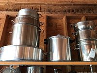 Wide view showing multiple large stainless steel stockpots stacked and placed on a shelf.
