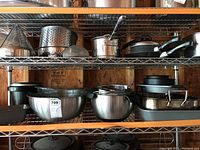 Shelves with an assortment of stainless steel mixing bowls, roasting pans, and cookware including pots and pans.