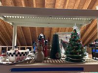 Photo showing wooden and ceramic Christmas decorations along with holiday dishware on a shelf under ceiling beams.