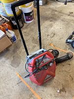 Overall view of the red Husky air compressor with handle and coiled hose attached, placed on concrete floor in workshop