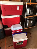 Photo showing four coolers stacked, three large and one smaller in front, all plastic, red and white colors.