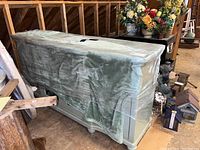 Entertainment cabinet covered with a green blanket and plastic wrap, showing general shape and size.